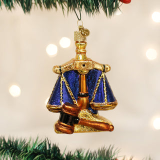 Decorative ornament of a gavel and scale on a Christmas tree with lights in the background