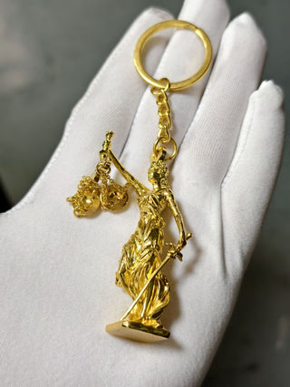 Gold keychain with a figure holding scales on a white hand