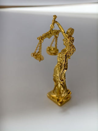 Gold statue of Lady Justice holding a scale on a white background