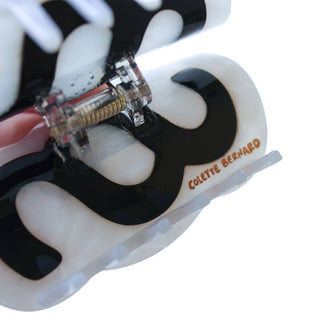 A close-up of a Colette Bernard claw hair clip made of glossy black and white patterned resin with a clear spring mechanism, on a white background.