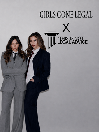 Two women posing in matching tailored business suits against a light gray background. One wears a light gray suit with a white shirt and dark tie, and the other wears a dark navy suit with a white shirt and red tie.