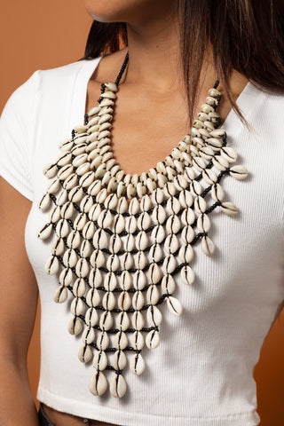 Necklace made of shell-like beads on a white top against a brown background