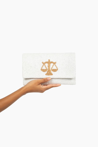 White clutch with gold emblem held by a hand on a white background