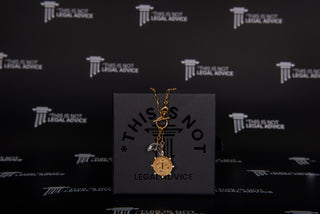 Gold necklace with a pendant on a black card with 'This is Not Legal Advice' text, against a matching background.