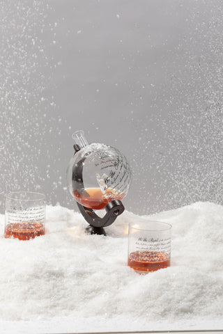 Cocktail setup with a spherical glass and two glasses on a snowy surface.