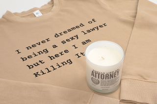 Beige sweatshirt with humorous text and a candle labeled 'Attorney' on a light background